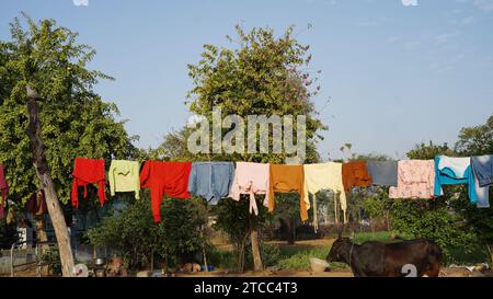 Dopo essere stato lavato, i vestiti colorati si asciugano su una linea di abbigliamento nel cortile esterno alla luce del sole. Stendibiancheria con abiti appena lavati all'aperto Foto Stock