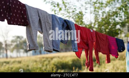 Dopo essere stato lavato, i vestiti colorati si asciugano su una linea di abbigliamento nel cortile esterno alla luce del sole. Stendibiancheria con abiti appena lavati all'aperto Foto Stock