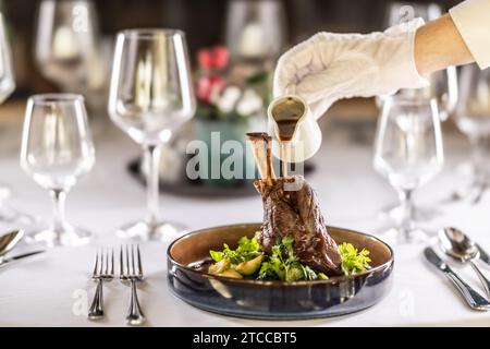 Lo chef o il cameriere termina il pasto direttamente sul tavolo del ristorante, versando la salsa sulla gamba di agnello confit. Foto Stock