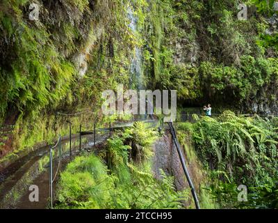 I turisti camminano attraverso la cascata a Levada do Rei PR18, il canale di irrigazione e le piante tropicali. Sao Jorge finisce alla fonte Foto Stock