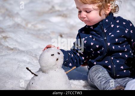Niña pequeña jugando con un muñeco de nieve por primera vez en hinvierno en la Vall de Núria Foto Stock