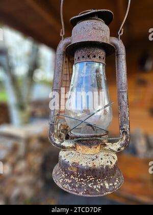 Un'antica lampada è sospesa su una parete esterna in un ambiente rustico Foto Stock