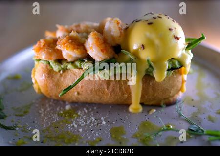 Uova Benedict. Muffin inglese con uova in camicia, prosciutto, lox, salmone, spinaci, avocado, formaggio e salsa Hollandaise. Servito con hash di patate. Antipasto classico da bistrot francese. Colazione o brunch Foto Stock