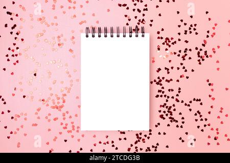 Mockup vuoto per appunti con cuori rossi metallizzati sparsi su uno sfondo rosa scintillante. Layout festivo. Foto Stock