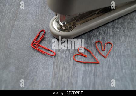 graffatrice con graffette rosse, due delle quali a forma di cuore, l'amore per l'ufficio Foto Stock