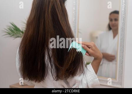 la donna pettina delicatamente i suoi capelli lunghi e sani, praticando la cura meticolosa dei capelli a casa. Foto Stock