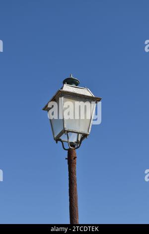 Una lanterna in acciaio corroso con pannelli di vetro nuvolosi su un palo arrugginito marrone Foto Stock