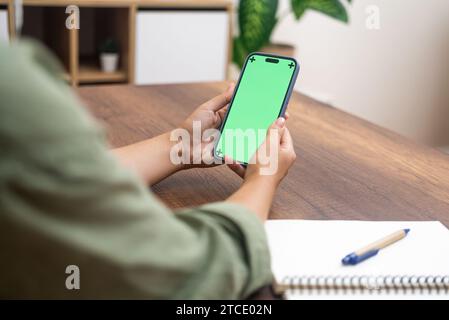 La giovane donna sceglie i prodotti che acquistano sul telefono cellulare seduto al tavolo del soggiorno Foto Stock