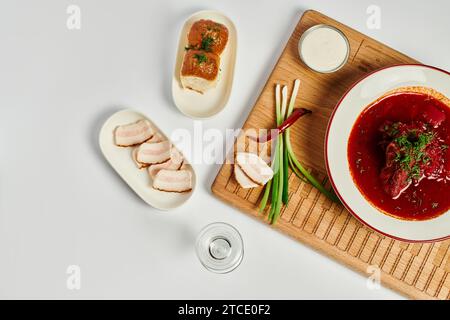 Borsch ucraino dal sapore ricco vicino a panini all'aglio, strutto di maiale e panna acida su tagliere di legno Foto Stock