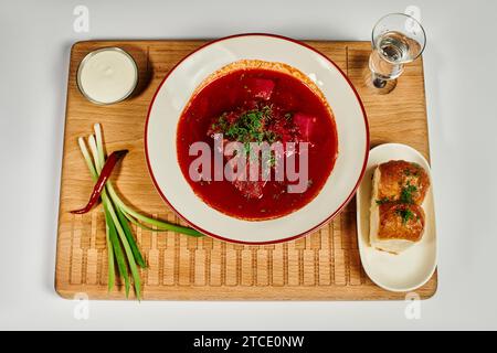 Tradizionale zuppa di borsch Ucraina con aneto fresco vicino ai panini all'aglio e panna acida su tagliere Foto Stock