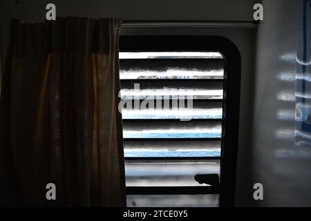 Luce che splende attraverso le tende di legno in una cabina della nave con una tenda gialla che blocca metà della luce Foto Stock