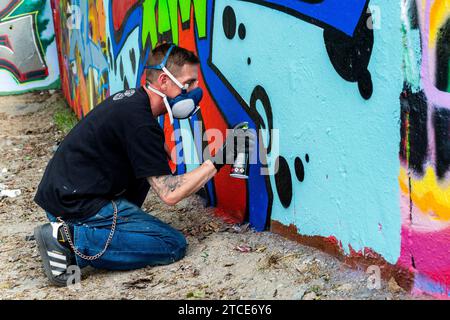 Berlino, Germania. Artista di graffiti che crea jet un'altra opera d'arte urbana su parti dell'ex muro di Berlino, al confine con l'ex Germania Est o DDR. Foto Stock