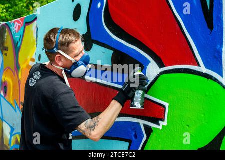 Berlino, Germania. Artista di graffiti che crea jet un'altra opera d'arte urbana su parti dell'ex muro di Berlino, al confine con l'ex Germania Est o DDR. Foto Stock