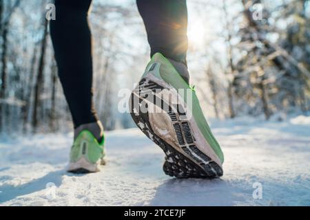 Suola da running immagine ravvicinata dei piedi da jogger invernali nelle sneakers da running che iniziano a correre sul sentiero innevato del parco durante la giornata di sole. Suola vista posteriore S Foto Stock