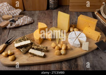 Formaggi assortiti su una tavola di legno, in stile rustico. Diverse varietà di formaggi a fette: parmigiano, tilsiter, halloumi con spezie, camembert, bocconc affumicato Foto Stock