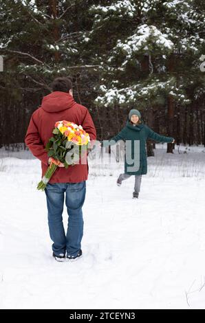 l'uomo tiene un grande mazzo di rose dietro la schiena, sullo sfondo davanti a lui c'è una donna felice innamorata. San Valentino in una foresta innevata o Foto Stock
