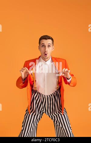 giovane pazzo e divertente con giacca arancione e pantaloni a righe su sfondo giallo. Foto Stock
