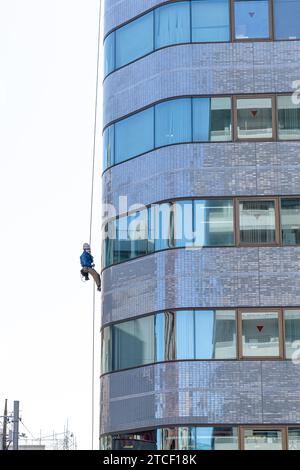 il lavoratore scende con una fune per eseguire la manutenzione di un edificio Foto Stock