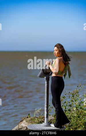 Windy Wind Blown Young Asian Woman Curvy Athletic Standing con San Francisco Bay sullo sfondo Foto Stock