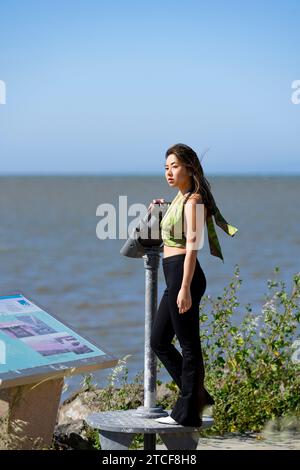 Windy Wind Blown Young Asian Woman Curvy Athletic Standing con San Francisco Bay sullo sfondo Foto Stock