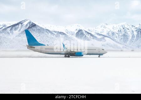 Un aereo di linea passeggeri si muove sulla pista in una violenta tempesta di neve sullo sfondo di alte montagne innevate Foto Stock