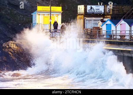 Regno Unito il tempo, la pioggia si cancella e le temperature iniziano a scendere a zero. L'ufficio Met dichiara avvisi di inondazione in tutto il sud dell'Inghilterra. Gli spettatori guardano dal lungomare mentre le onde si infrangono. Un intrepido bodyboarder non è perturbato dalle onde guidate dal vento che si avvicinano al buio e all'acqua ghiacciata di Towan Beach Newquay Cornwall UK. 12 dicembre 2023, Robert Taylor / Alamy Live News. Foto Stock