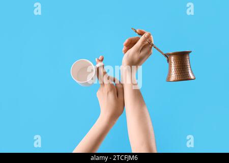 Mani femminili che tengono cezve e tazza di caffè su sfondo blu Foto Stock
