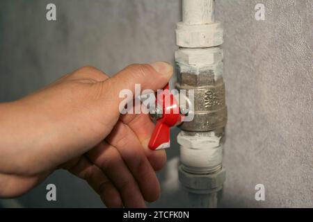 Un proprietario di casa con tute blu sta usando una chiave per chiudere la valvola a sfera argentata su un tubo di riscaldamento, interrompendo efficacemente l'erogazione di calore a un ra della casa Foto Stock