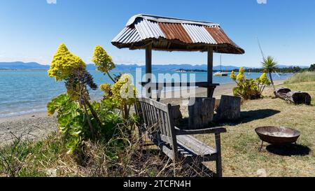 Un bar esterno con sgabelli a tronco d'albero e tetto in ferro ondulato sul lungomare di Motueka, il Motueka Sandspit sullo sfondo, isola sud, Tasman Foto Stock