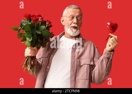 Uomo maturo con bouquet di rose e mongolfiera a forma di cuore per San Valentino su sfondo rosso Foto Stock