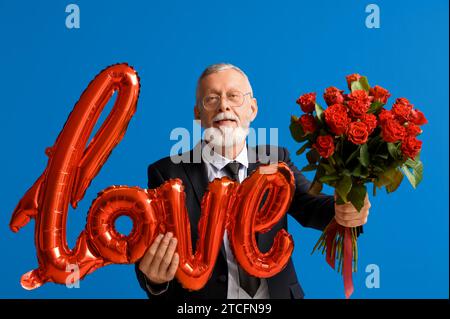 Uomo maturo con bouquet di rose e mongolfiera a forma di AMORE per le parole su sfondo blu. Festa di San Valentino Foto Stock