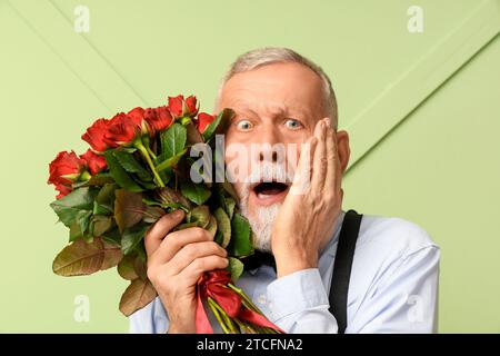 Uomo maturo scioccato con bouquet di rose su sfondo verde. Festa di San Valentino Foto Stock