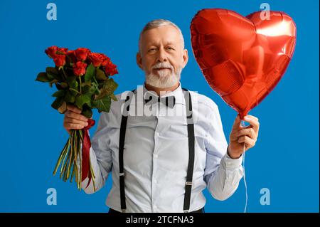 Uomo maturo con bouquet di rose e palloncino a forma di cuore su sfondo blu. Festa di San Valentino Foto Stock