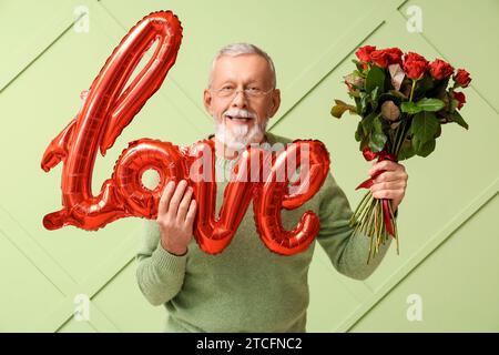 Uomo maturo con bouquet di rose e mongolfiera a forma di AMORE per le parole per San Valentino su sfondo verde Foto Stock