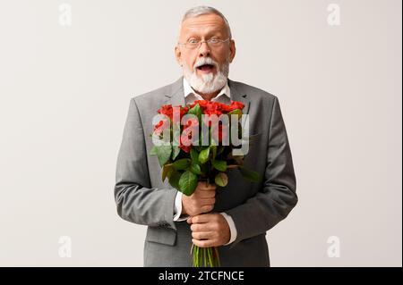 Uomo maturo scioccato con bouquet di rose su sfondo bianco. Festa di San Valentino Foto Stock