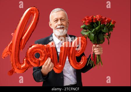 Uomo maturo con bouquet di rose e mongolfiera a forma di AMORE per le parole per San Valentino su sfondo rosso Foto Stock