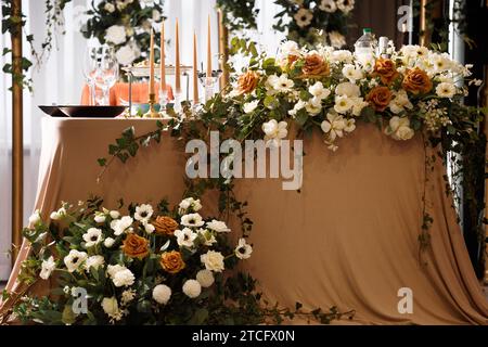 Tavolo per matrimoni festivi per gli sposi, decorato con composizioni di fiori freschi e candele. Decorazioni nuziali. Festeggiamenti nel banchetto Foto Stock
