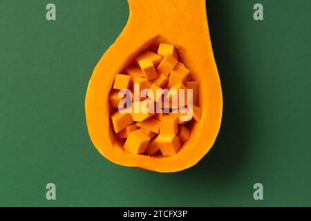 Metà di una zucca dolce all'arancia e zucca a dadini all'interno su sfondo verde, vista dall'alto. Verdure sane, vegetarianismo. Foto Stock