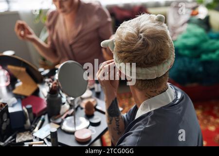 Vista posteriore di un giovane che si trucca e guarda allo specchio che si prepara per lo spettacolo notturno, spazio per le copie Foto Stock