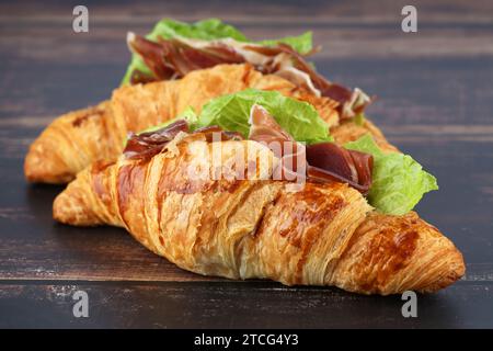 Panini con croissant con prosciutto e lattuga su tavola di legno. Foto Stock