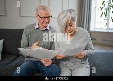 Triste stanco, deluso, coppia di anziani di mezza età siedono con un documento cartaceo. Infelice anziano maturo donna che legge banconote che gestiscono le finanze bancarie calcolano le tasse pianificazione prestito pagamento pensione Foto Stock