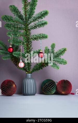 Vaso grigio con rametto di abete e decorazioni in carta dell'albero di Natale su sfondo grigio. Biglietto d'auguri, concetto di Capodanno. Vista frontale. Foto Stock