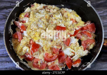 Uova strapazzate con pomodori, un piatto a base di uova mescolate, montate o sbattute insieme mentre vengono riscaldate delicatamente, con sale, burro, olio e pe nero Foto Stock