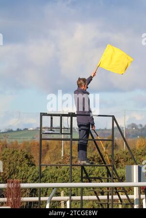 Gara di caccia nazionale del Regno Unito con bandiera gialla che inizia la corsa di cavalli sotto gli ordini dell'ippodromo Down Royal Racecourse, Lisburn, Irlanda del Nord. Foto Stock