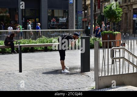 Un uomo che si rinfrescava e si lavava il viso con acqua fresca proveniente da una fonte d'acqua pubblica in una calda giornata estiva nel centro di Bruxelles Foto Stock