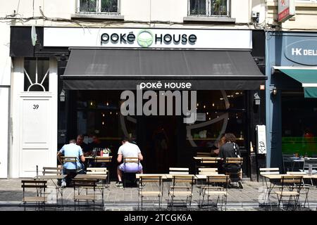 Persone sedute su piccole sedie fuori dall'entrata del ristorante hawaiano "Poké House" nel centro della città di Bruxelles Foto Stock