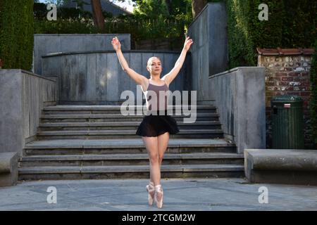 Giovane donna con top viola e gonna nera che esegue una posa di balletto su una superficie di pietra di fronte alle scale Foto Stock