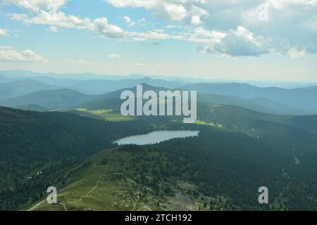 Vista di uno stretto sentiero dalla cima che scende lungo il pendio fino a un lago in una pittoresca valle di montagna sotto un cielo estivo nuvoloso. Parco naturale Ergaki, K. Foto Stock