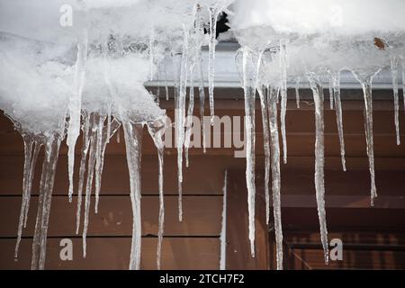 Ghiaccioli cristallini e luccicanti che si sono formati a causa delle condizioni climatiche gelide, appesi al bordo di una residenza in legno marrone Foto Stock