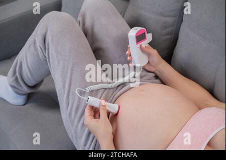 Primo piano della pancia di una donna incinta usando un doppler domestico. Schermo vuoto. Foto Stock